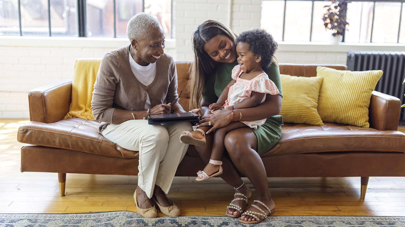 African American woman sits and laughs with her daughter and granddaughter inside of her Erickson apartment home.