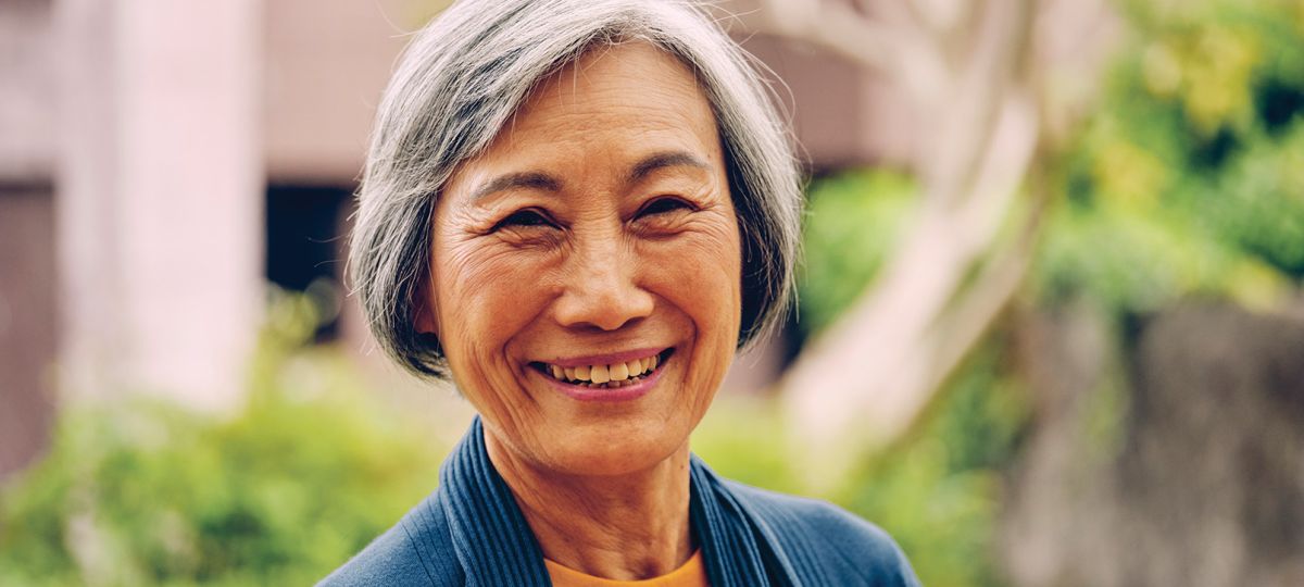 Smiling older lady in a garden surrounded by vibrant flowers and greenery.